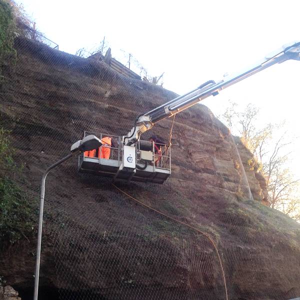 A crane is lifting a roll of rockcon mesh for installation.